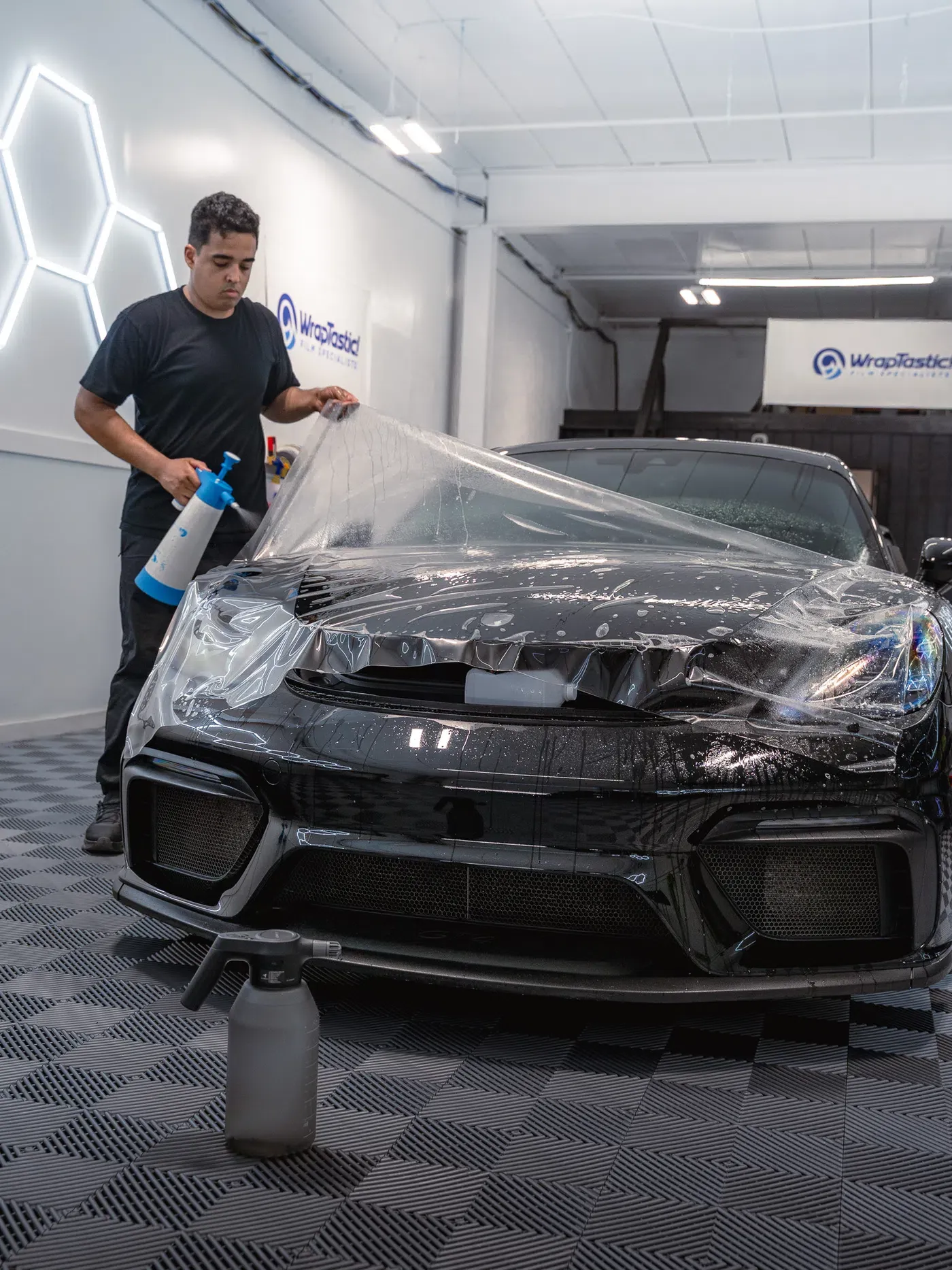A WrapTastic installer positioning clear paint protection film over a black sports car