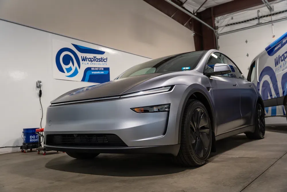 A gray electric car in a WrapTastic workshop beside a branded service van
